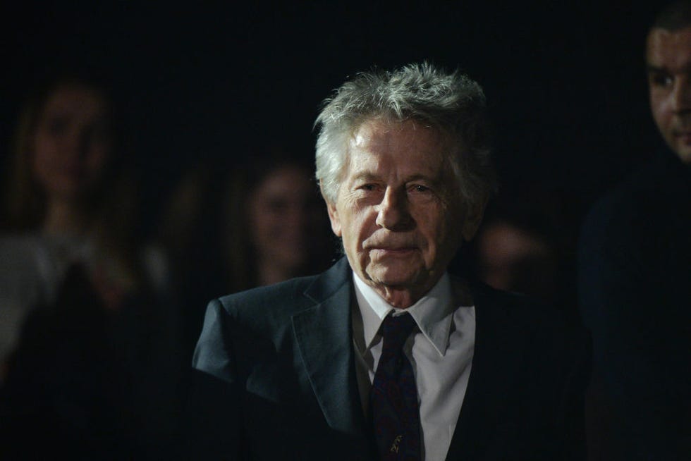 roman polanski walks in a gray suit jacket, white dress shirt and dark colored tie