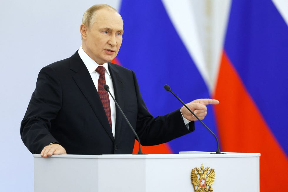 vladimir putin pointing with his left hand as he speaks at a podium