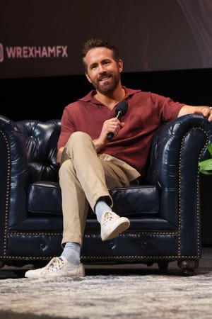 ryan reynolds sitting in a chair and smiling while holding a microphone