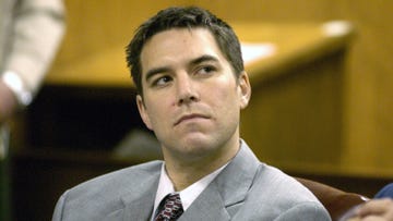 scott peterson looks over his left shoulder, he wears a gray suit jacket, white collared shirt and red patterned tie