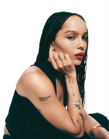 person with braided hair sitting with their hand on their face showcasing various tattoos