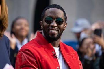 sean diddy combs smiles at the camera, he wears a red jacket over a white shirt and circular sunglasses