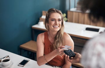 shot of an attractive young woman sitting and using her credit card to pay at a cafe