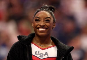 simone biles smiling while wearing a usa uniform at a gymnastics meet