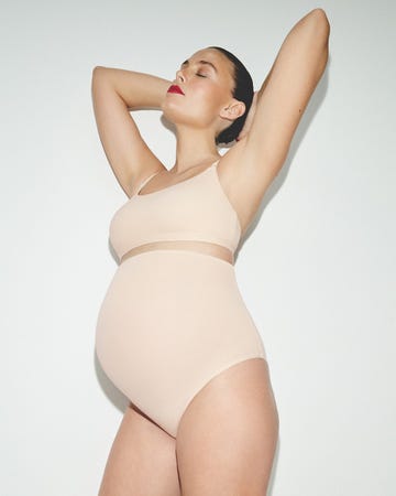 a pregnant person posing with arms raised in a minimalistic setting