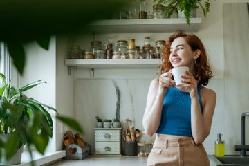 smiling young woman standing with coffee cup at home