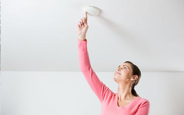 a woman checking smoke alarm in a home