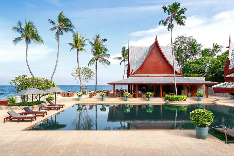 a pool with lounge chairs and umbrellas by a building with palm trees chiva som health retreat thailand