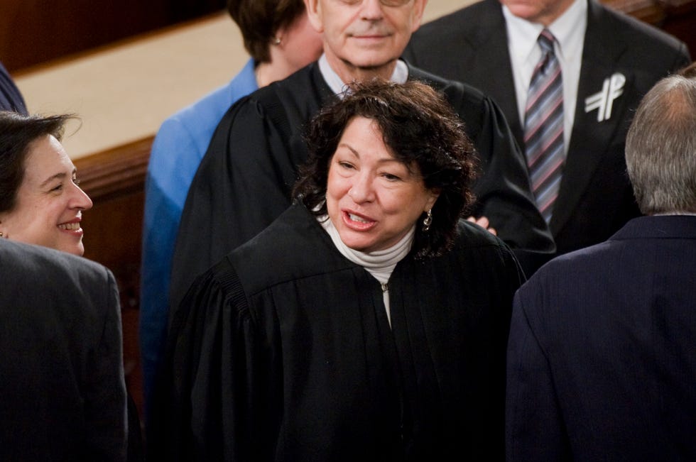 sonia sotomayor, wearing black judge robes, speaking to someone off camera in the middle of a crowded room