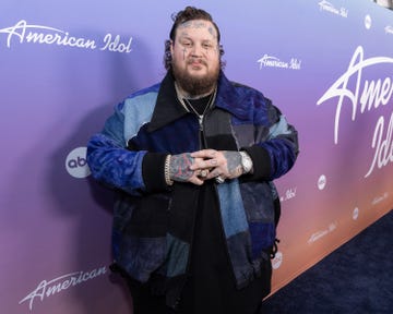 jelly roll crossing his hands while smiling for a photo in front of an american idol backdrop