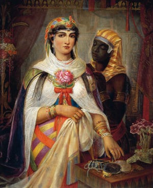 cleopatra vii wears a colorful head piece, pearl jewelry and a white scarf with a floral bouquet in front of her chest