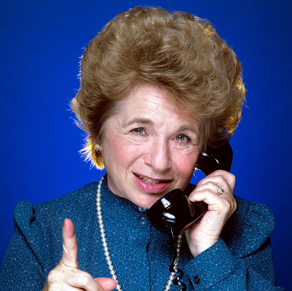 dr ruth westheimer holds a telephone to one ear and points a finger toward the camera with her other hand