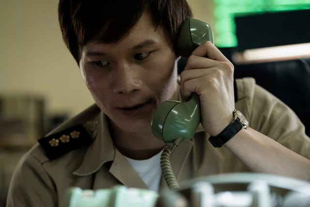 actor hoa xuande holding a cord phone to his left ear with a concerned look on his face in a scene from the sympathizer