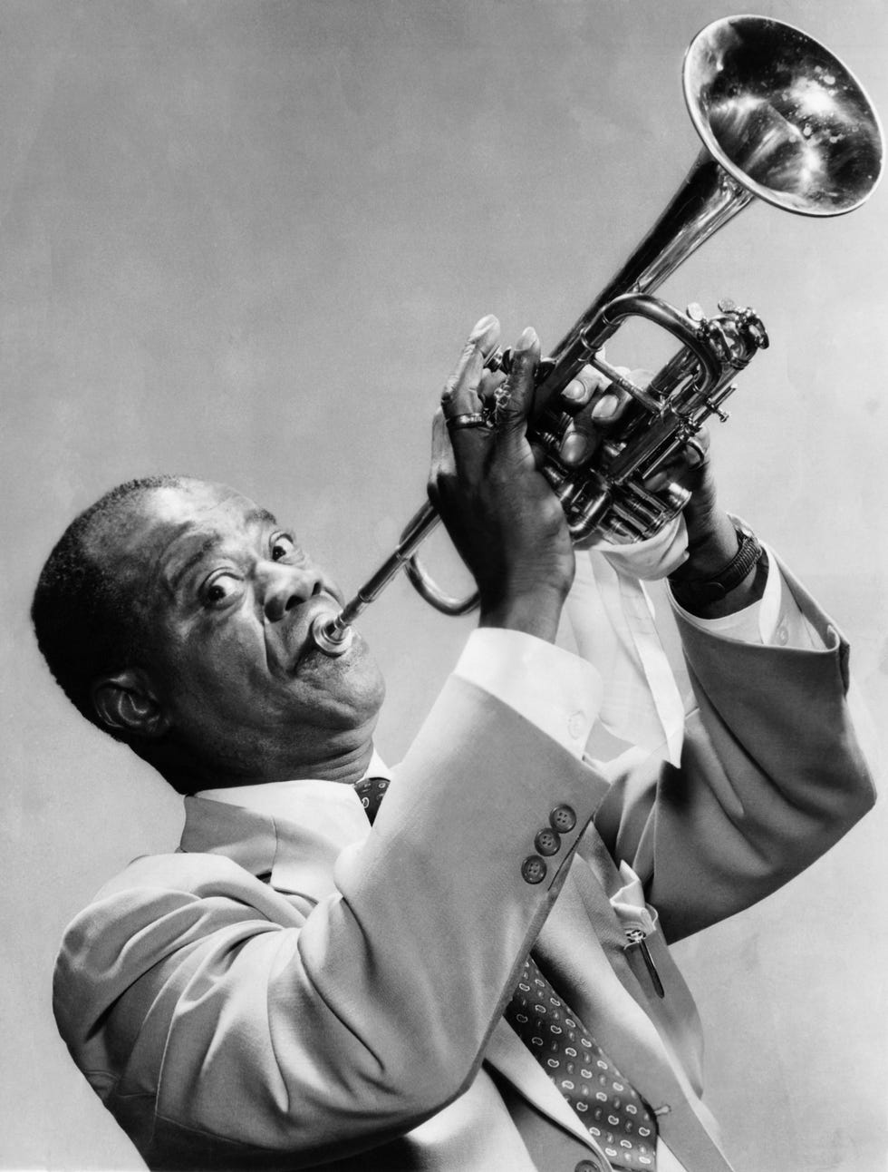 louis armstrong looking ahead toward a camera as he plays a trumpet