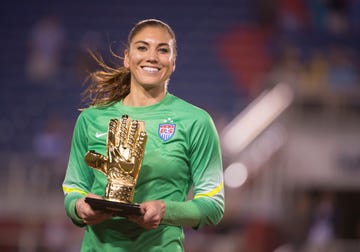 hope solo smiles and holds trophy, she wears a green longsleeve jersey