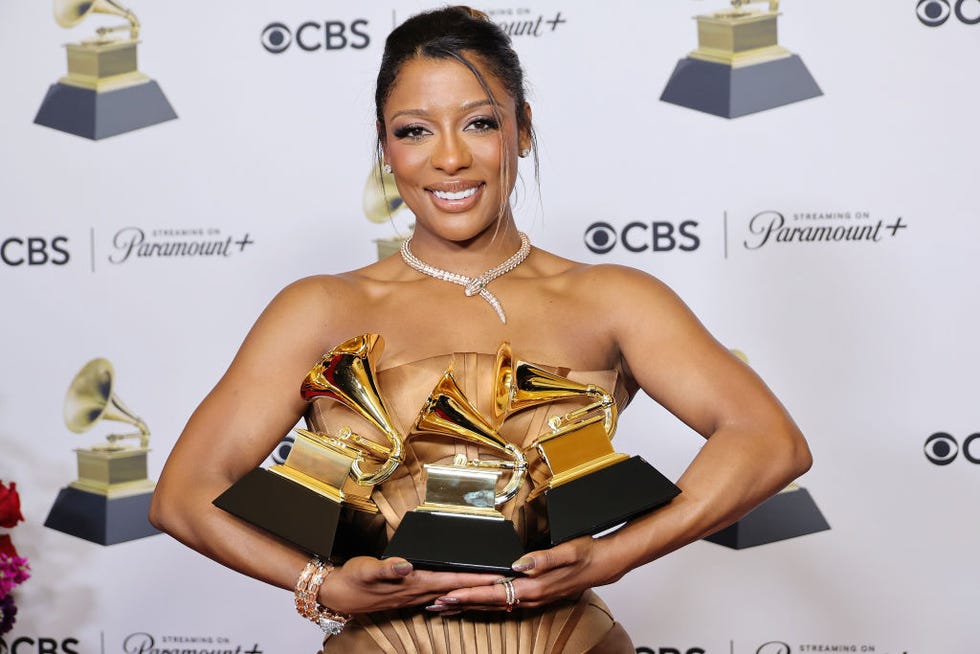 victoria monet holding three grammophone trophies across both hands and smiling for a photograph