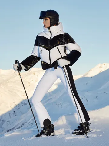 a model wearing a black and white jacket and pants by goldbergh on a snowy mountain while holding ski poles in a roundup of the best womens ski jackets 2024