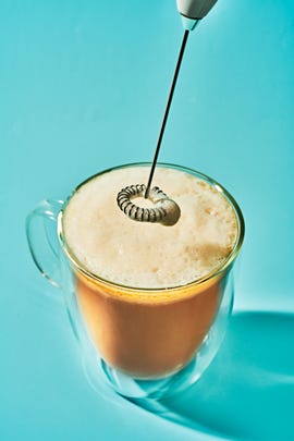 coffee in a clear mug, with a frother hovering above