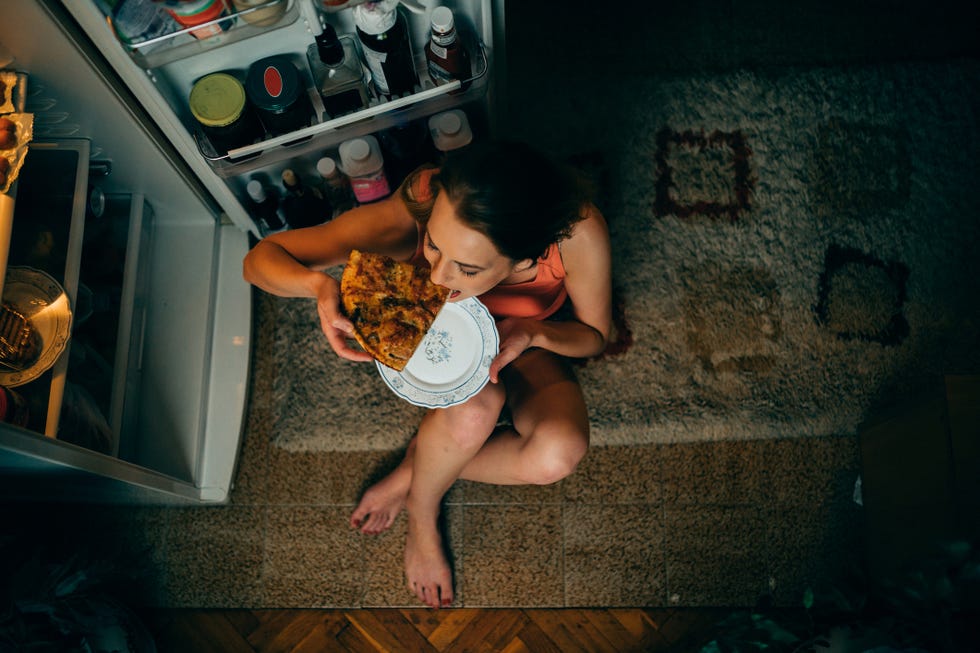 woman eating in front of the refrigerator in the kitchen late night