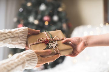 woman in sweater giving a wrapped christmas gift box to child glowing snow bokeh, fir tree winter holidays