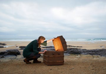 woman looking inside treasure chest on deserted beach