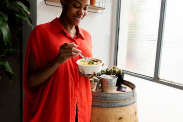 woman standing at home eating bowl of salad