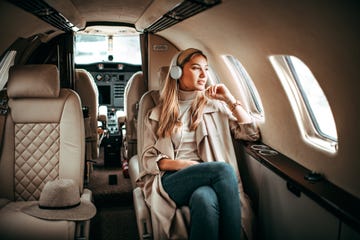 young fashionable woman sitting on a private airplane and listening to music through headphones