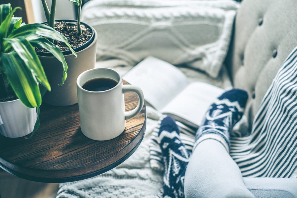 young woman enjoying coffee and relaxing on a sofa with a book