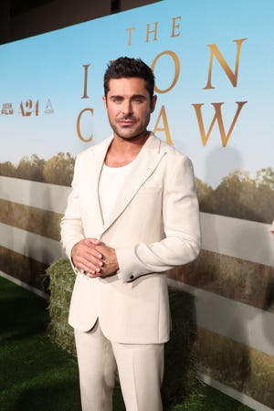 zac efron stands and looks at the camera in a cream colored suit over a white shirt