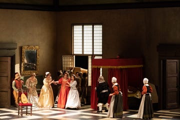 the setting features several characters in period clothing, engaged in lively conversation a red canopied bed is positioned prominently, while a mirror hangs on the wall, reflecting part of the scene a woman in a bright red dress stands at the center, while others in the background appear to be moving furniture the flooring has a contrasting black and white pattern, enhancing the room's historical ambiance