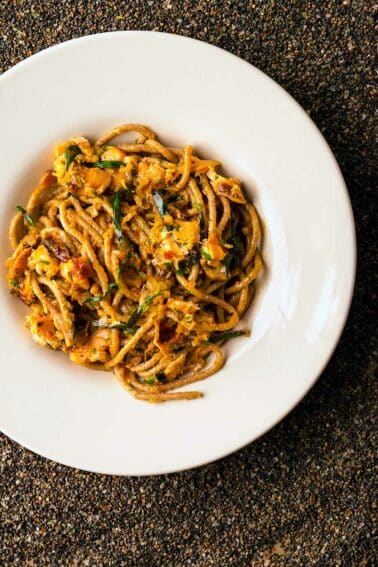 A plate of smoked salmon pasta on black sand.