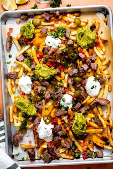 Baking tray topped with carne asada fries loaded with meat, cheese, guacamole, jalapeños, pico de Gallo, and sour cream.