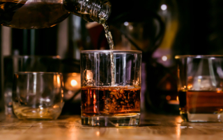 Several glasses of brown liquor on a table represent increased alcohol use.