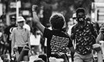 Black and white photo. Center: a person in a black tshirt and afro hair.