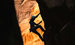 Photograph of a person climbing a canyon. The person is in the middle of the route, heading to the top.