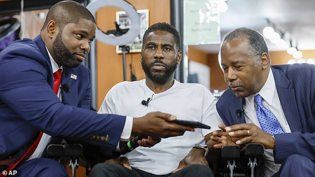 Donalds holds the phone for Dr. Ben Carson as he talks with Trump on speakerphone over Rocky's Barbershop owner