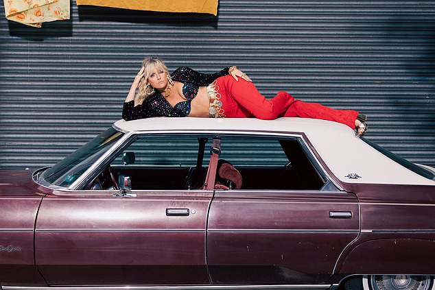 She put on a confident display as she posed on top of a vintage car in the edgy ensemble while shooting the video