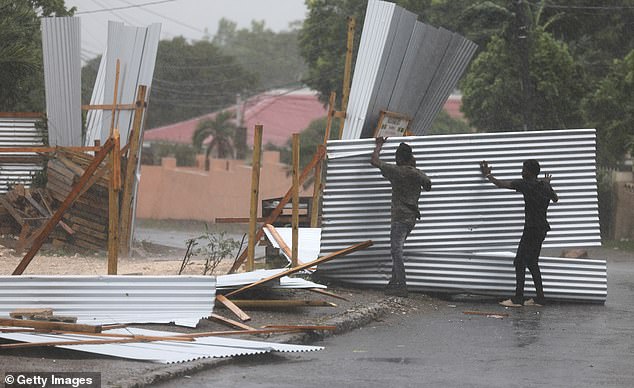 The historic hurricane, however, has only weakened slightly, packing a 140 mph punch on residents of Kingston, seen here trying to save pieces of a tin face split apart by the weather