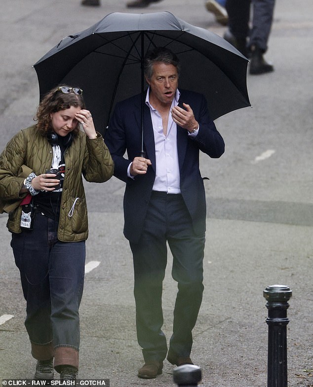 Grant keeps dry under a brolly, and makes heavy weather of munching a snack, during a break from filming