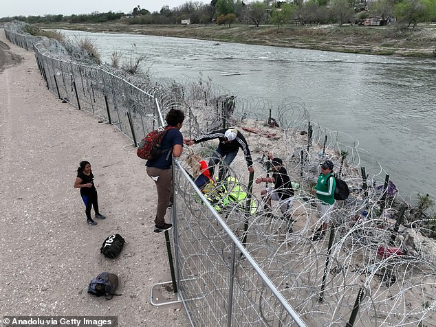 A group of illegal migrants scale a fence near Eagle Pass, Texas