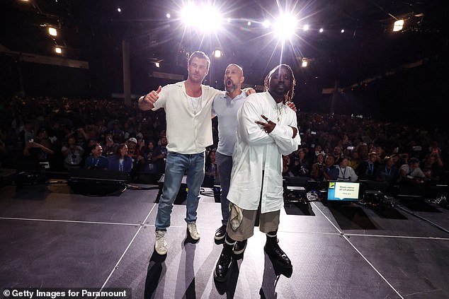 Hemsworth hit the stage in Hall H of the San Diego Convention Center donning a white t-shirt under a white button-down short-sleeved shirt with a long gold chain