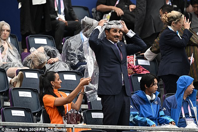 A spectator in the crowd pulls on a plastic poncho to protect from the rain