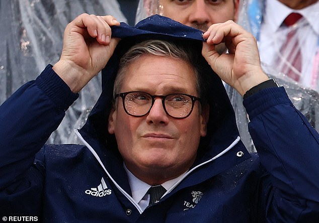 Prime Minsiter Keir Starmer protects from the rain wearing a Team GB rain coat