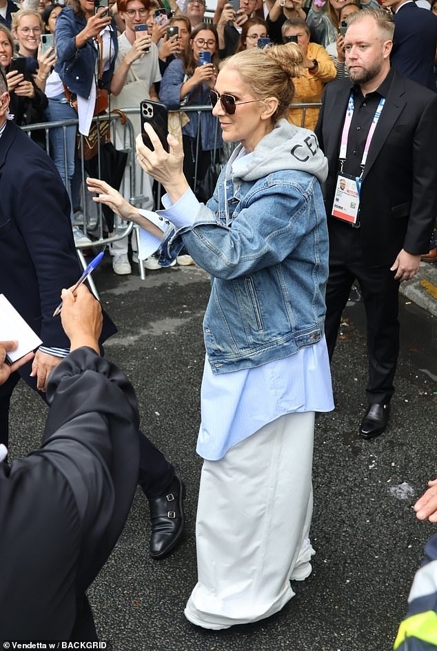 Cutting a casual figure in flared white linen trousers, a blue shirt and a grey hoody which she layered under a denim jacket