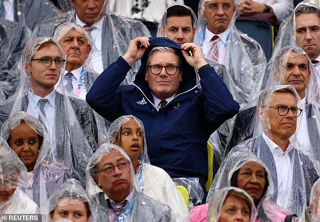 PM Keir Starmer pulls on his raincoat to protect from the rain