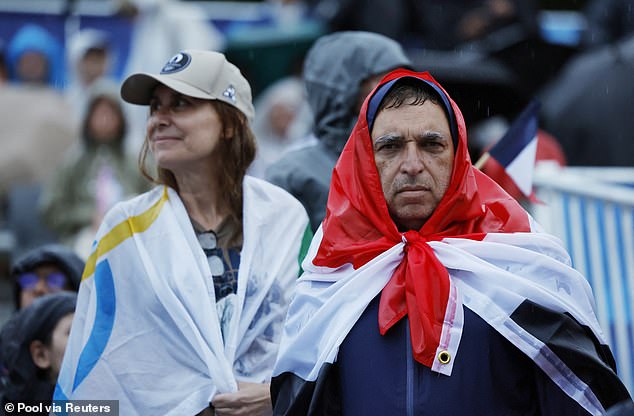 A spectator covers his head with a flag to protect from the miserable onslaught of rain in Paris