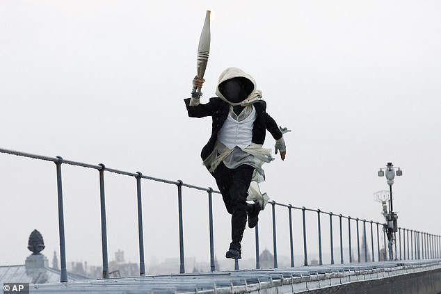 A masked torch bearer runs atop the Musee d'Orsay, in Paris, France, during the opening ceremony