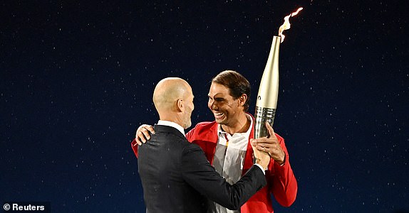 Paris 2024 Olympics - Opening Ceremony - Paris, France - July 26, 2024. Former footballer Zinedine Zidane passes the Olympic torch to tennis player Rafael Nadal during the opening ceremony. REUTERS/Dylan Martinez