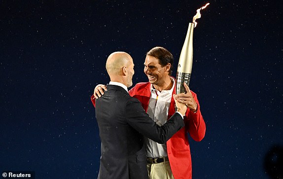 Paris 2024 Olympics - Opening Ceremony - Paris, France - July 26, 2024. Former footballer Zinedine Zidane passes the Olympic torch to tennis player Rafael Nadal during the opening ceremony. REUTERS/Dylan Martinez