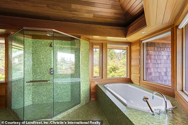 A large bathroom (pictured) is decked out in wood and sage green tiles along the floor and in the glass walk-in shower